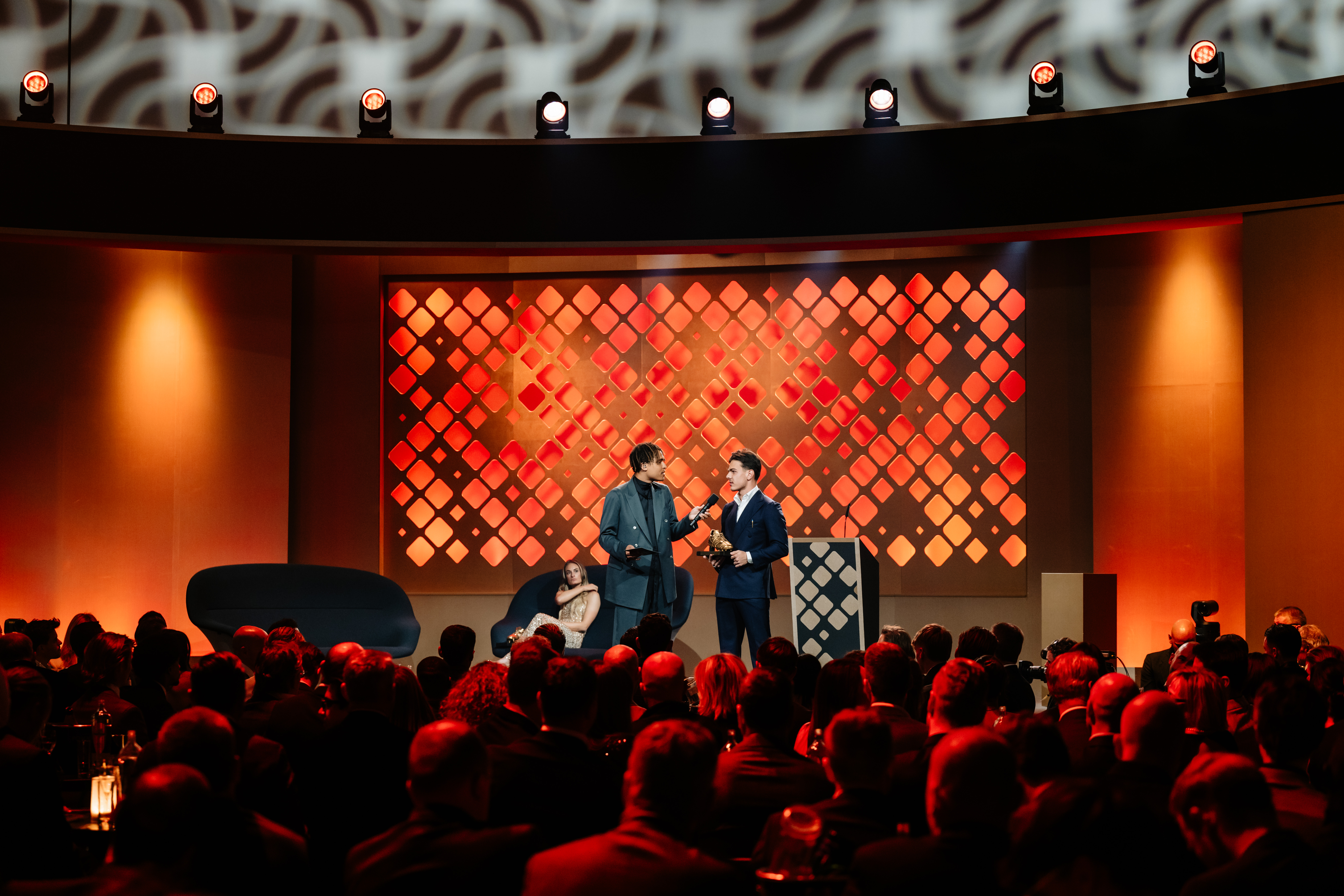 Podium van de Gouden Schoen voor een lichtwand met ruitpatroon in oranje en rood